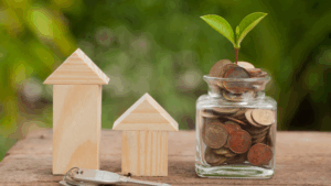 a glass jar with coins and a small house with a plant growing out of it